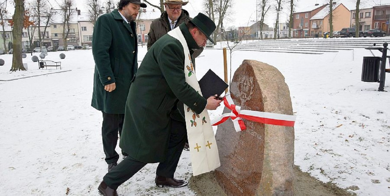 Tablica usytuowana jest naprzeciwko pamiątkowej alei drzew wzdłuż ciągu komunikacyjnego przy ulicy Plac Wolności. Oba elementy spinają w całość tradycję związaną z łowiectwem w naszym regionie